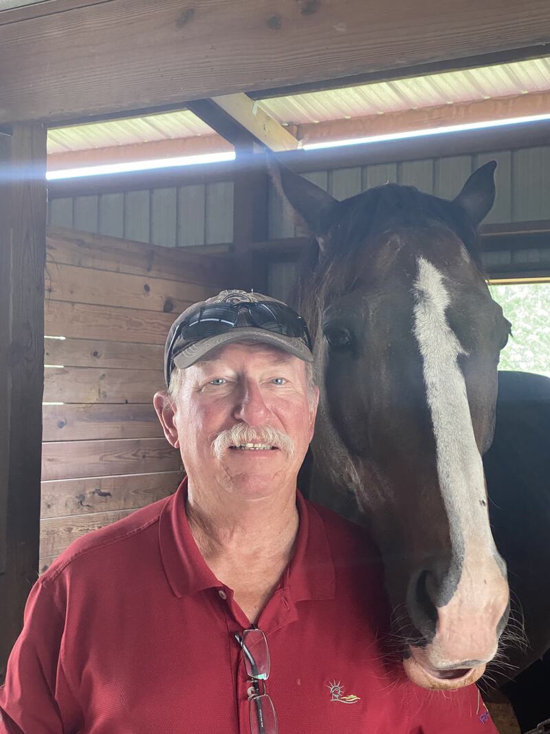 Older white man, Duncan, standing next to horse smiling at camera.